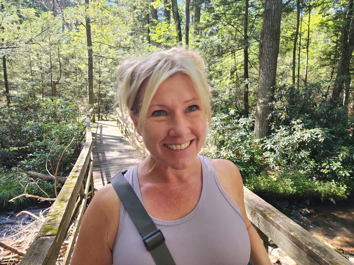 Kelly, founder of Meraki Roots, smiling on a wooded trail bridge